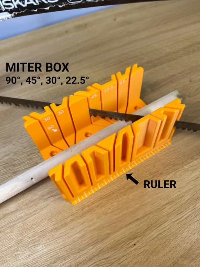 A 3D printer created miter box on a wooden surface with a saw and a wooden dowel. It is functional and cool.