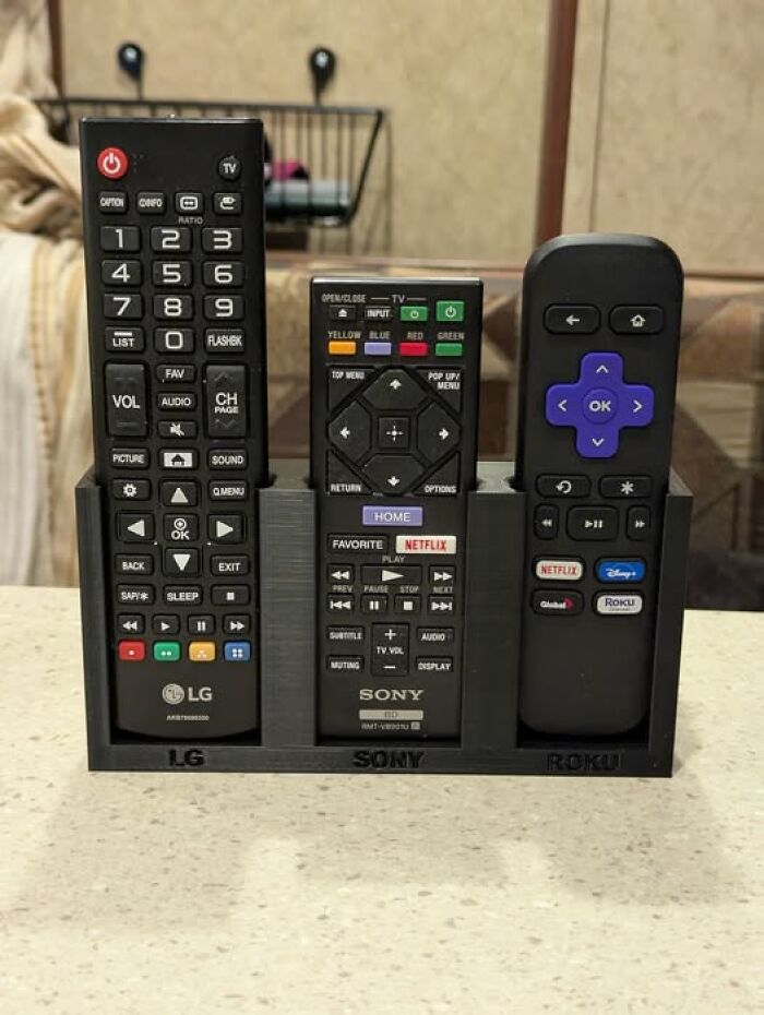 A 3D printer created remote control holder with three remote controls on a table. It is functional and cool.