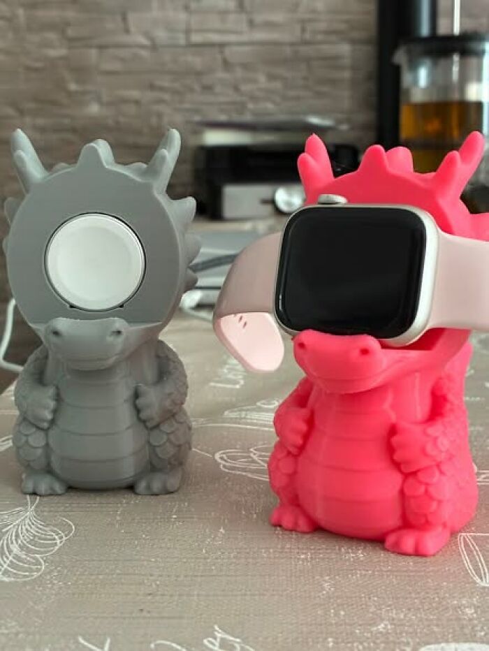 Two functional 3D printer created dragon-shaped Apple Watch stands, one grey and one pink, holding smartwatches.