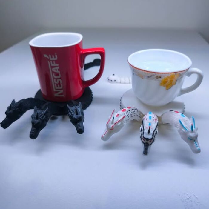 Two unique 3D printer created dragon-themed cup holders, one with a red Nescafé mug and one with a teacup.