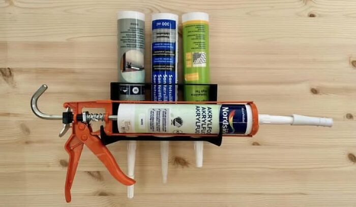 A wall-mounted 3D printed holder for a caulk gun and sealant tubes, showcasing cool and functional things created using a 3D printer.