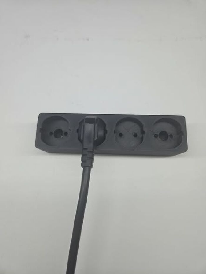 A black 3D printed power strip with three outlets and one plug inserted, illustrating functional and cool things made with a 3D printer.