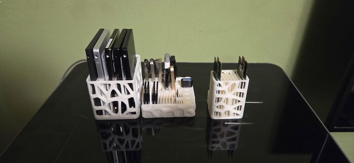 Three white, intricately patterned organizers filled with electronics and cards, functional things created using a 3D printer.