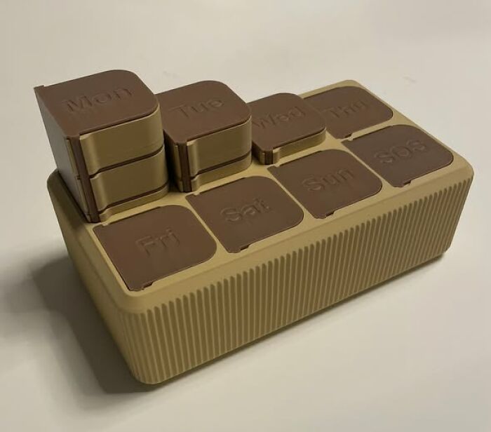 A brown and tan weekly pill organizer, a cool thing created using a 3D printer, with days of the week.