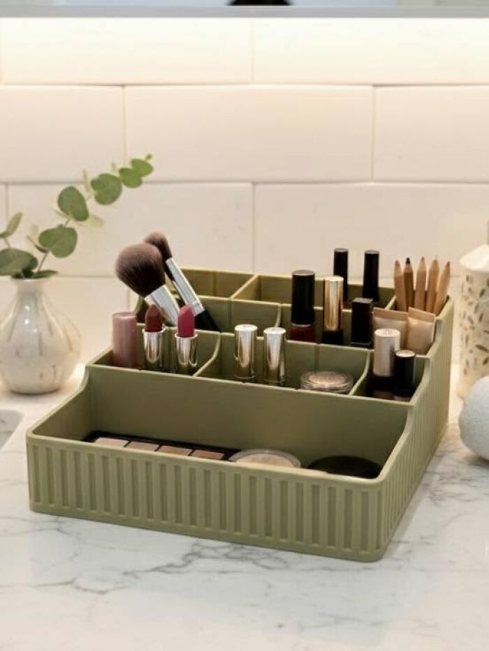 A green makeup organizer, a functional thing created using a 3D printer, filled with cosmetics on a counter.
