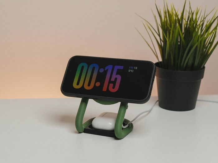 A smartphone charging on a green and black stand, a cool thing created using a 3D printer, displaying time.