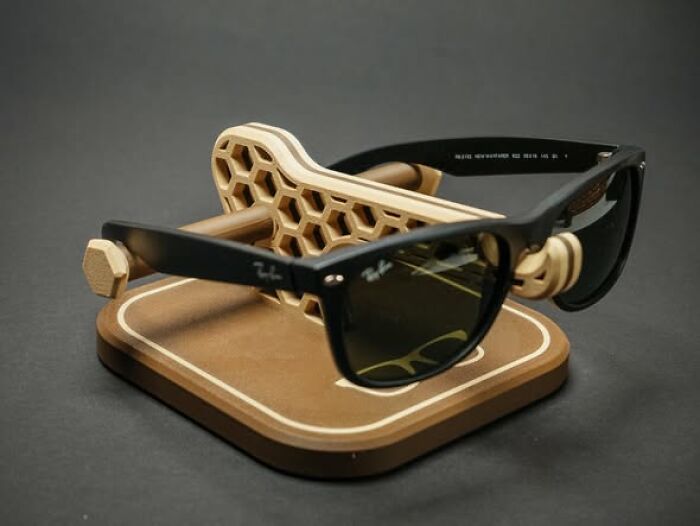 A pair of black sunglasses resting on a hexagonal, wooden-patterned stand, a cool thing created using a 3D printer.
