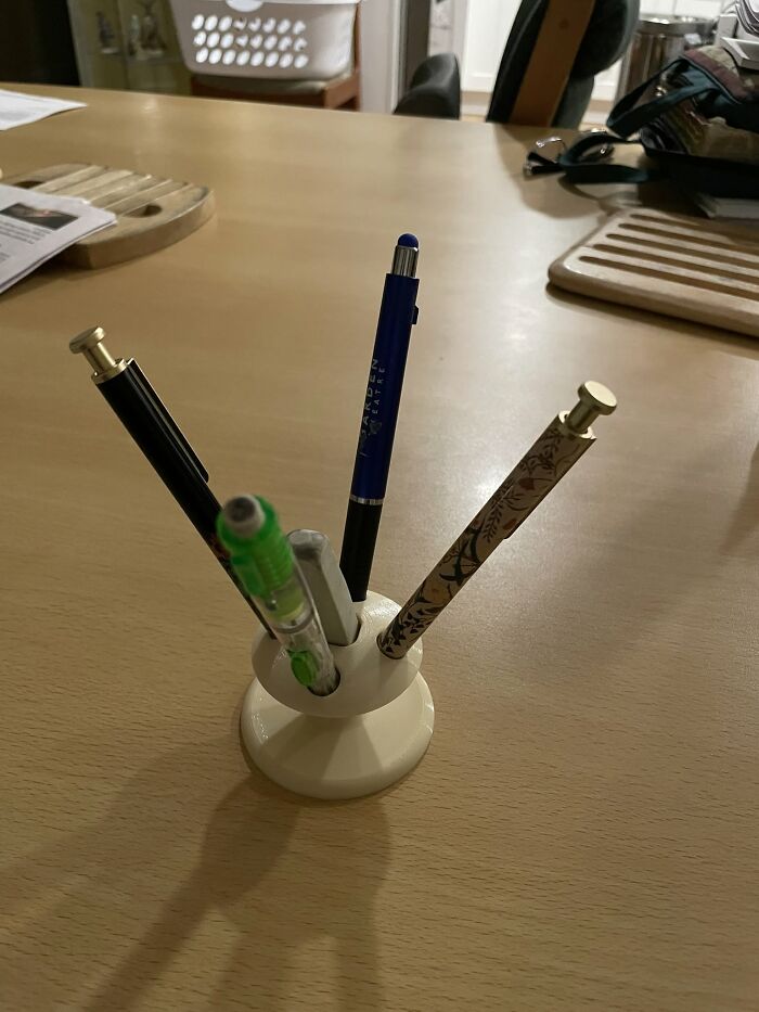 A 3D printed pen holder keeps multiple pens organized on a wooden table, showcasing functional 3D printer creations.