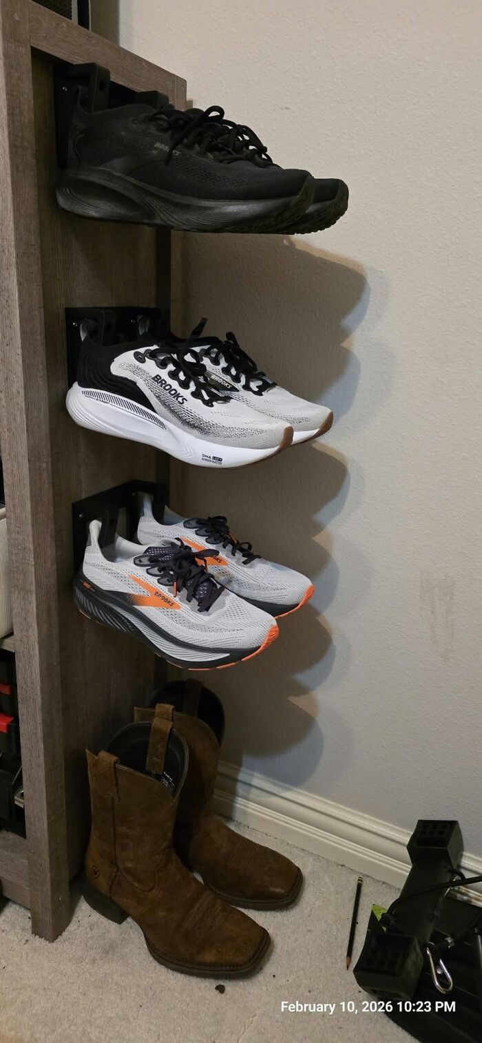 Various shoes, including sneakers and cowboy boots, organized on a wall-mounted rack, a functional item created using a 3D printer.