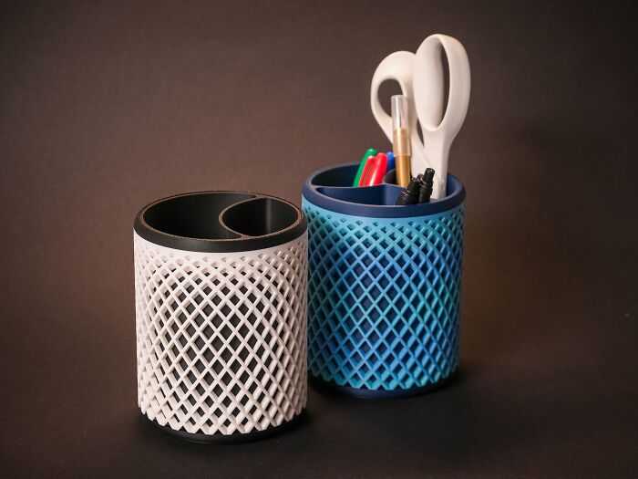 Two textured cylindrical holders, one white and one blue, containing pens and scissors, cool things created using a 3D printer.