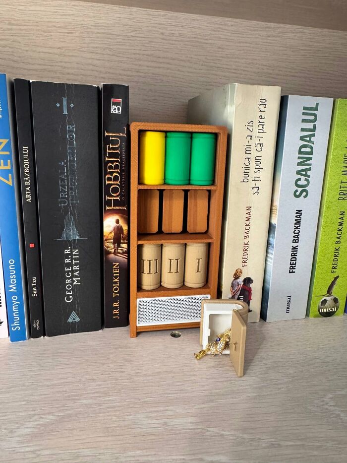 A miniature wooden-look 3D printer created bookshelf with tiny books and a small open safe, next to full-sized books.