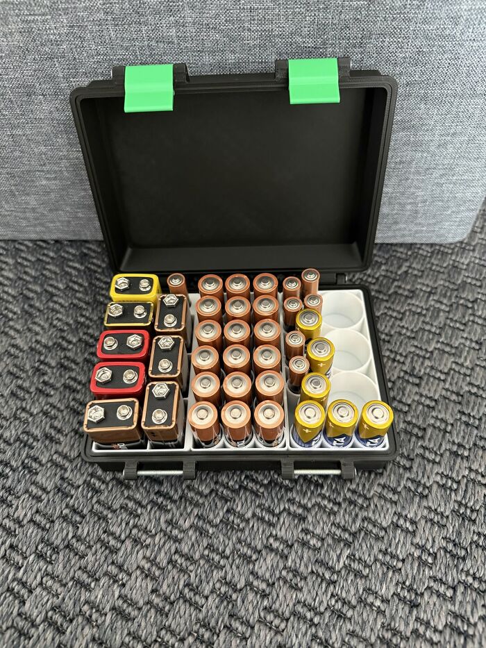 An open black storage case, 3D printed with green latches, neatly organizes various battery sizes.