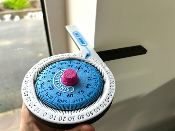 A hand holding a white and blue 3D printer created protractor tool with various measurements and a pink center.