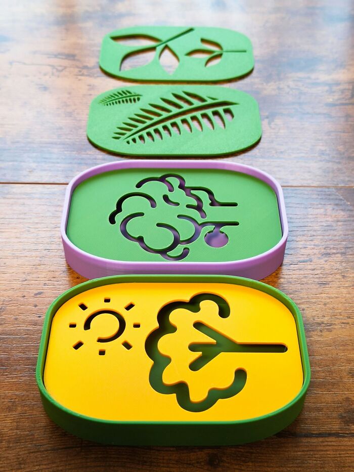 A stack of colorful, 3D printed soap dishes with nature-inspired cutouts, including a leaf and sun.