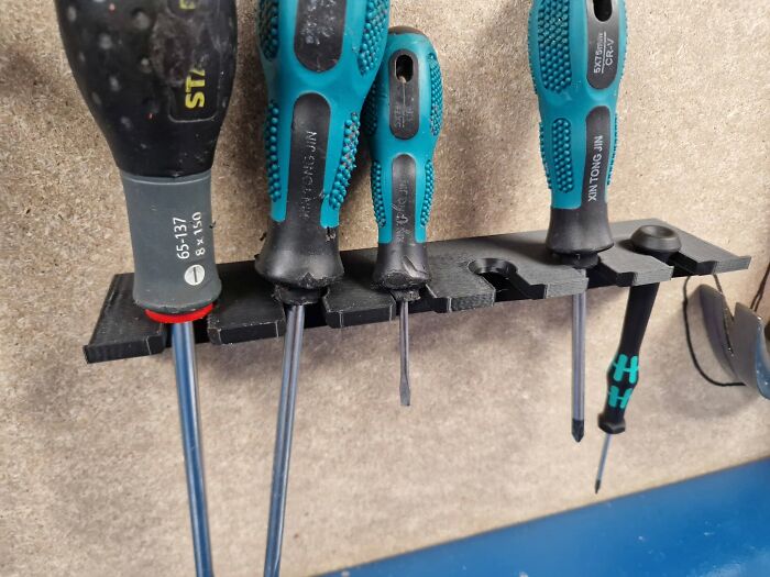 A black, 3D printer created tool holder with various screwdrivers neatly organized on a wooden surface.