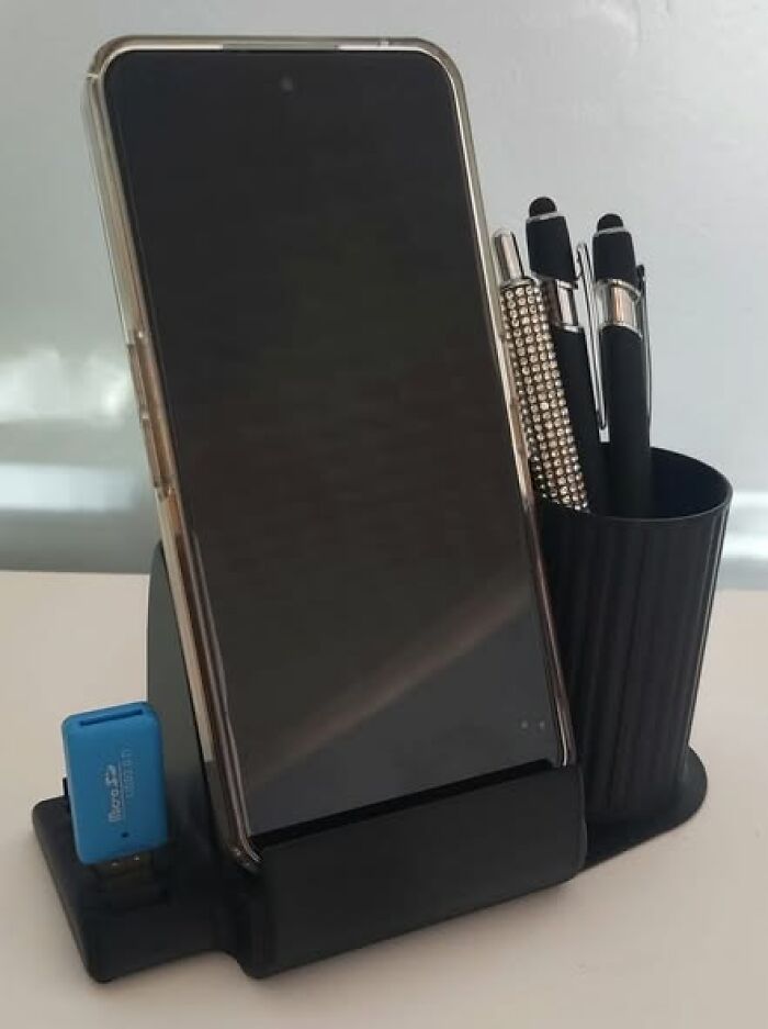 A functional 3D printed desk organizer holds a smartphone, pens, and a USB drive, keeping a workspace tidy.