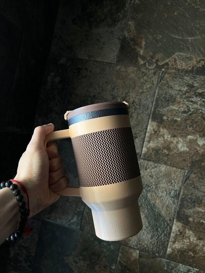 A hand grips a stylish 3D printed travel mug with a textured brown and black design, perfect for beverages.