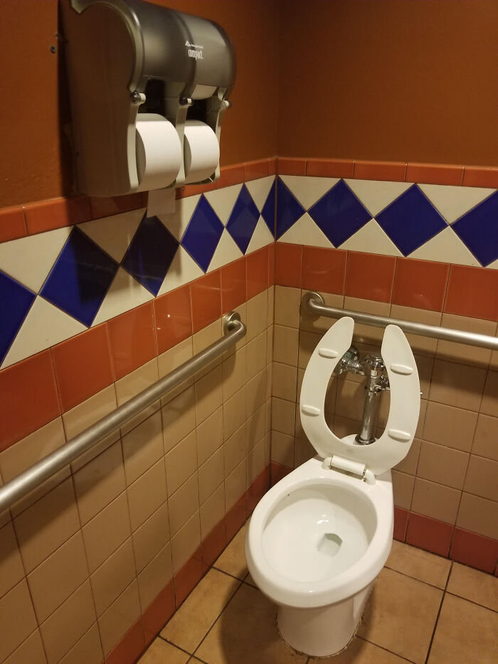 A terribly designed public bathroom with a toilet and grab bars, featuring blue and orange diamond-patterned tiles.