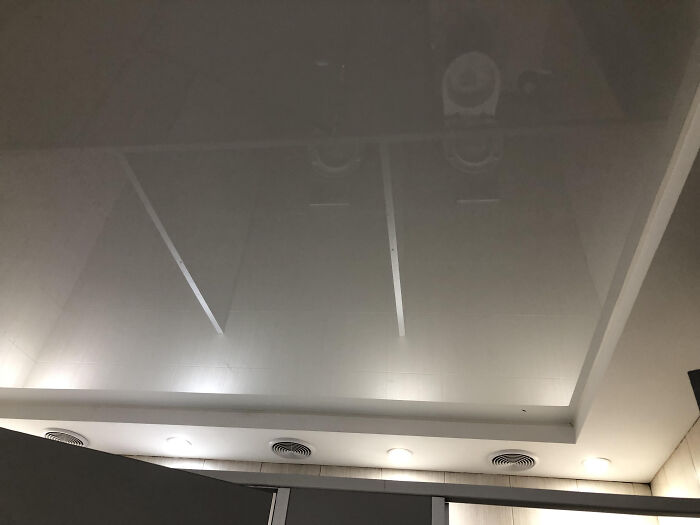 A reflective ceiling shows the terrible design of a public bathroom with ventilation grilles.