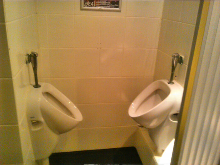 Two urinals are placed very close to each other in a public bathroom, a terribly designed bathroom.