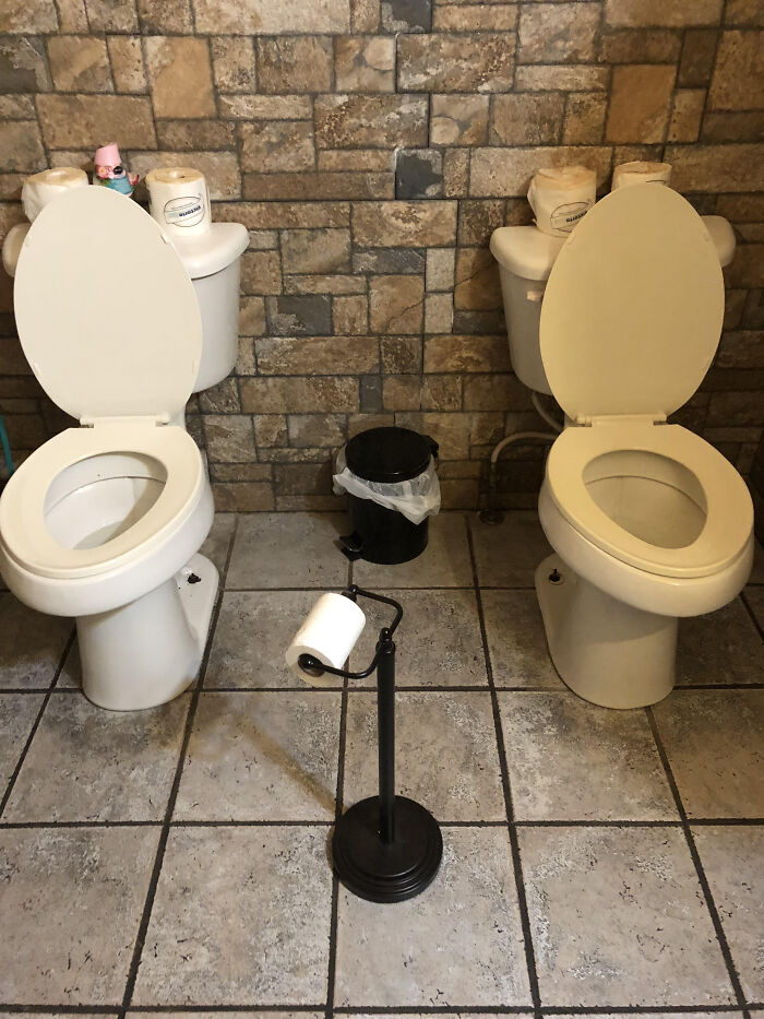 Two terribly designed bathrooms side-by-side without privacy, showcasing a shared toilet setup with a stone wall.