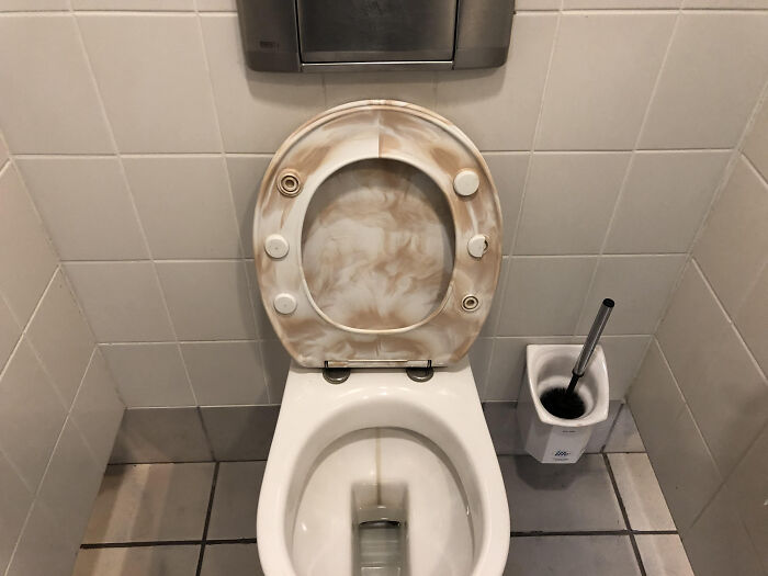 A terribly designed bathroom toilet with a stained and dirty seat, emphasizing poor hygiene and maintenance.