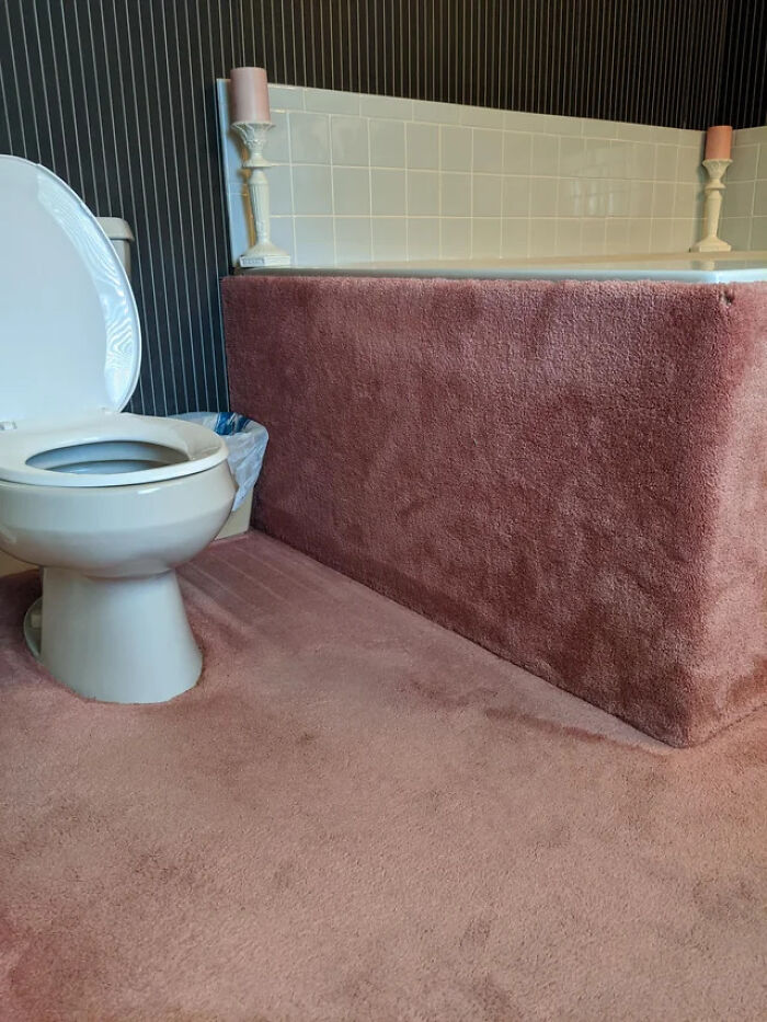 A terribly designed bathroom featuring a toilet next to a pink carpeted bathtub and matching carpeted floor.