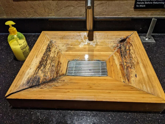 A terribly designed wooden bathroom sink with noticeable water damage and mold, next to a bottle of soap.