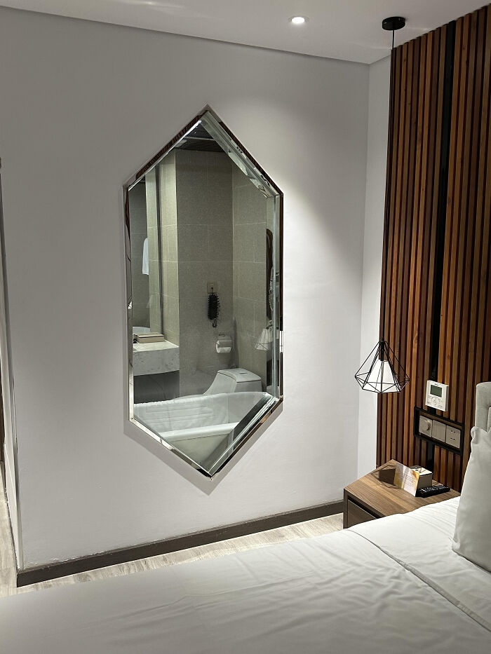 A mirror in a hotel room reflecting a badly designed bathroom with a toilet and bathtub.