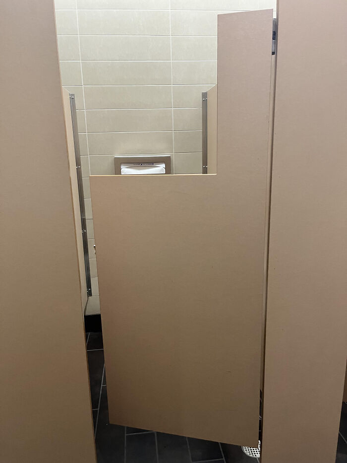 A bathroom stall door that is too short, revealing the toilet inside, an example of terribly designed bathrooms.