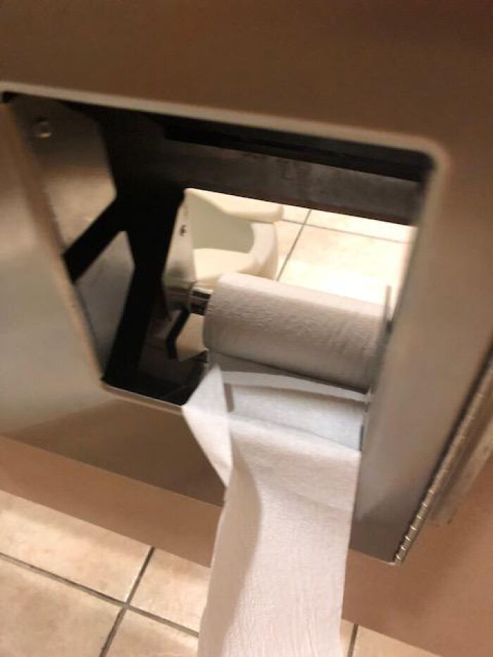 A close-up of a partially used roll of toilet paper in a dispenser, showcasing a terribly designed bathroom.