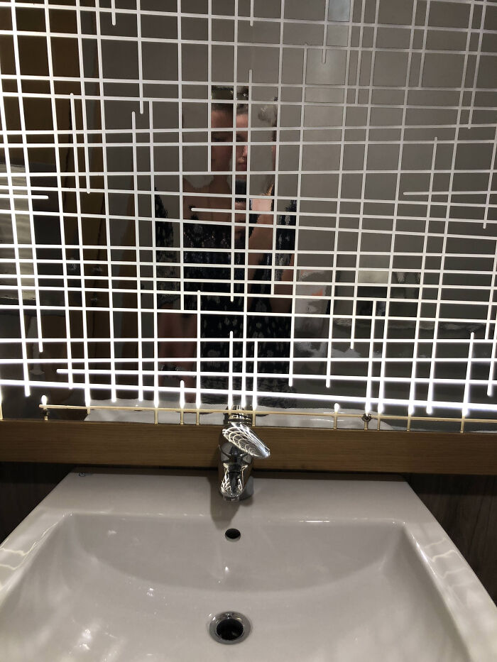 A reflection of a person taking a photo in a mirror over a sink, demonstrating a terribly designed bathroom.