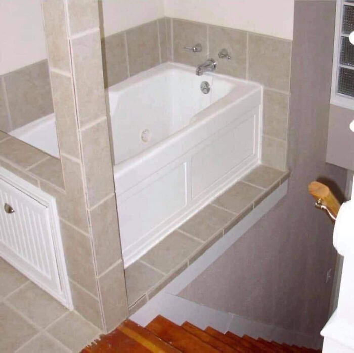A terribly designed bathroom with a bathtub positioned dangerously at the edge of a staircase, creating a fall hazard.