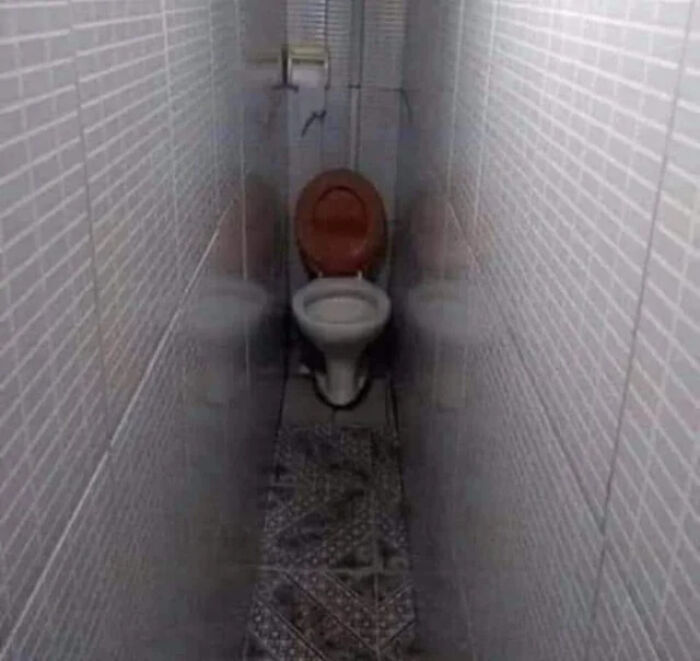A terribly designed bathroom featuring a toilet crammed at the end of a very long, narrow, tiled corridor.