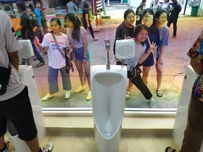 A terribly designed bathroom with urinals facing a clear glass window, visible to people outside, offering no privacy.