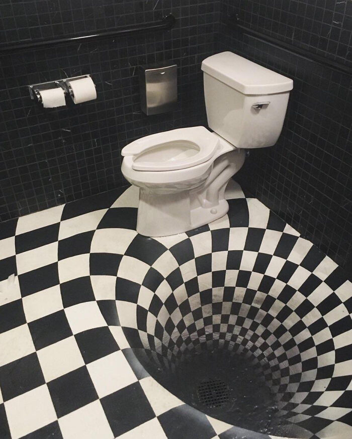 A dizzying terribly designed bathroom with a toilet on a black and white checkerboard floor creating an optical illusion.