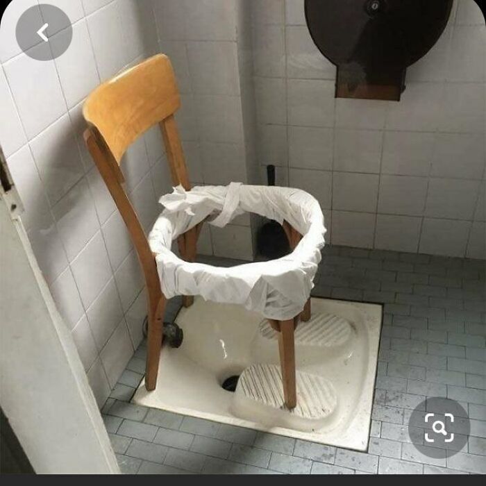A strangely designed bathroom with a wooden chair modified into a makeshift toilet over a squat toilet base.