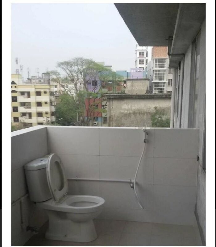 A poorly designed bathroom with a toilet installed on an outdoor balcony, overlooking city buildings.