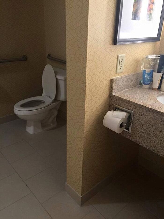 A terribly designed bathroom with a toilet awkwardly placed behind a wall, making it difficult to access the toilet paper.