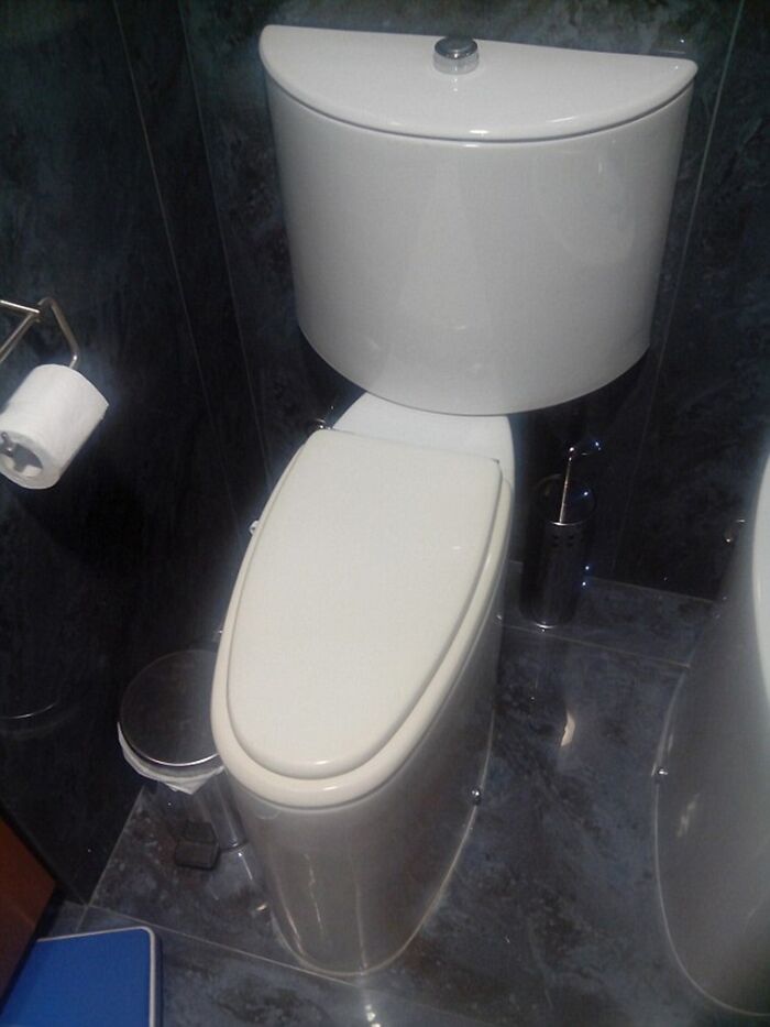 A compact, terribly designed bathroom with a wall-mounted toilet and a dark tiled background, showing a bad design.