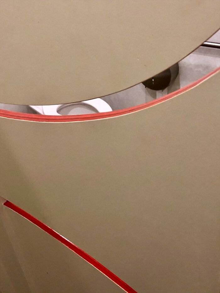 A poorly designed bathroom with a curved stall wall revealing the toilet, highlighting terribly designed bathrooms.