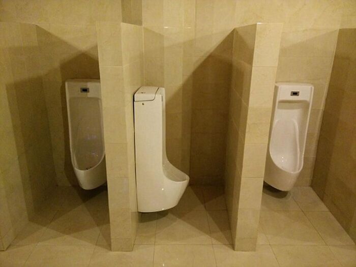 A public bathroom featuring three urinals, one unusually tall, contributing to the collection of terribly designed bathrooms.