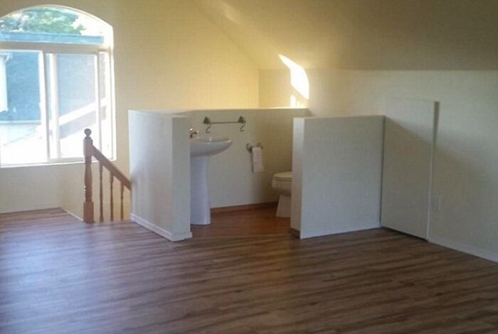 An open-concept attic bathroom with a sink and toilet behind short partitions, an example of terribly designed bathrooms.