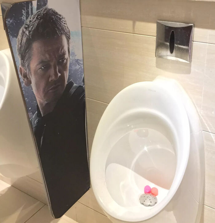 A bizarre bathroom design featuring a urinal next to a cut-out of Matt Damon, one of many terribly designed bathrooms.