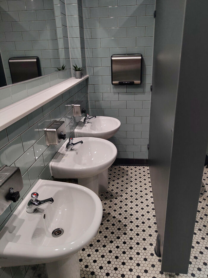 A poorly designed public bathroom with three sinks in a row and a small mirror, highlighting terribly designed bathrooms.