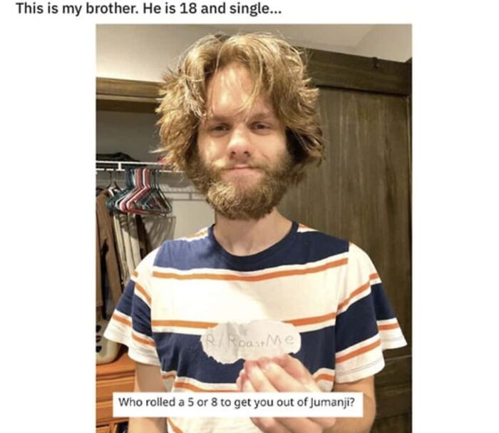A man with a beard and shaggy hair holds a sign, with a clever clapback about being from Jumanji.