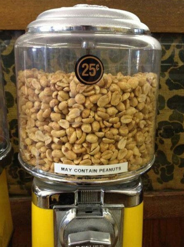 A hilariously failed sign on a clear gumball machine filled with peanuts states, May Contain Peanuts, with a 25-cent label.