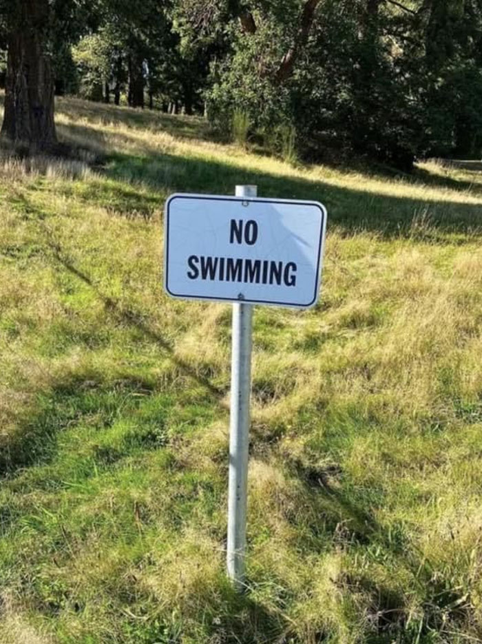A hilariously failed sign in a grassy field states NO SWIMMING, with no water in sight.
