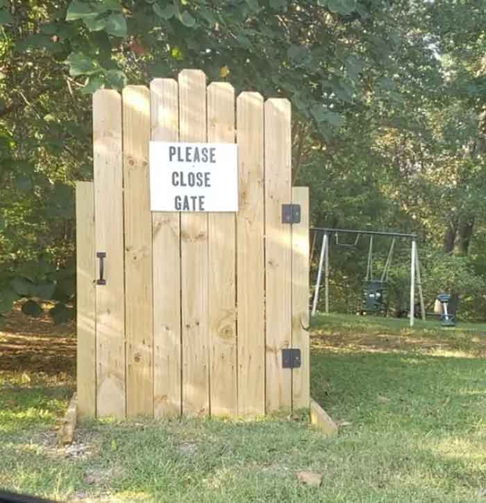 A hilariously failed sign reading PLEASE CLOSE GATE on a wooden gate that is not closed and has a large gap.