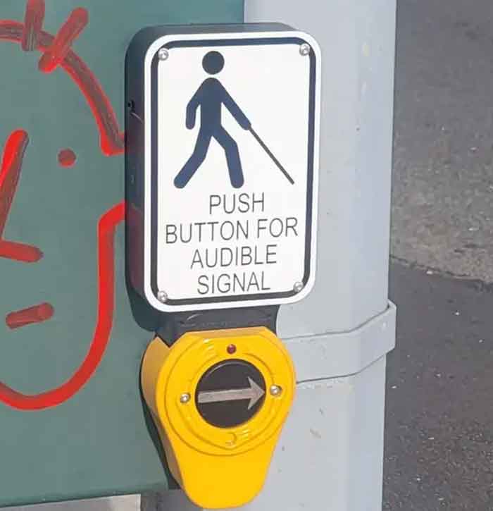 A crosswalk sign that hilariously failed, depicting a person with a cane with an arrow pointing right for an 'audible signal'.